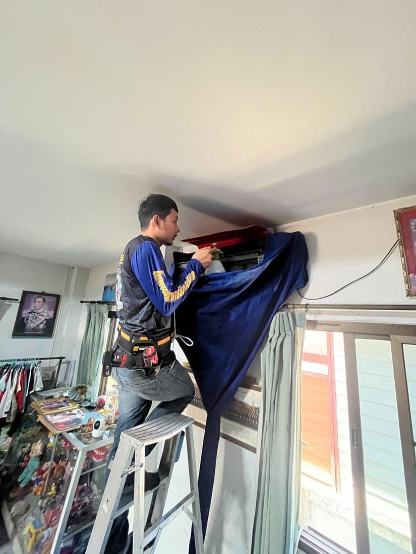 ช่างขึ้นบันไดล้างแอร์ในห้องนอน โดยขึงผ้ากันน้ำสีแดงรองใต้ตัวเครื่อง