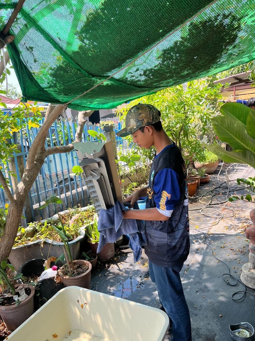ช่างล้างชิ้นส่วนกลางสวนใต้ตาข่ายพรางแสงสีเขียว มีกะละมังรองน้ำอยู่ข้างตัว