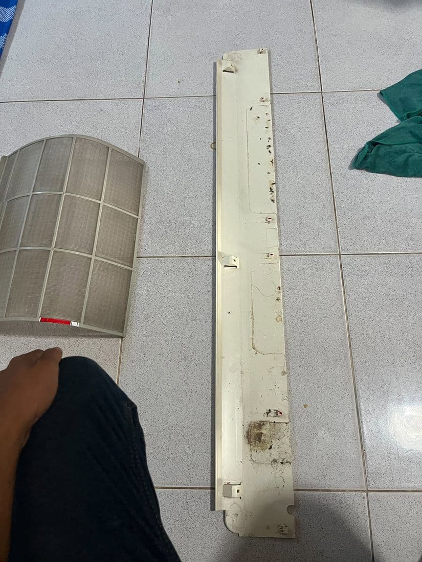 แผ่นกรองและชิ้นส่วนแนวยาววางบนพื้นกระเบื้อง ช่างกำลังเอื้อมมือหยิบขึ้นมา