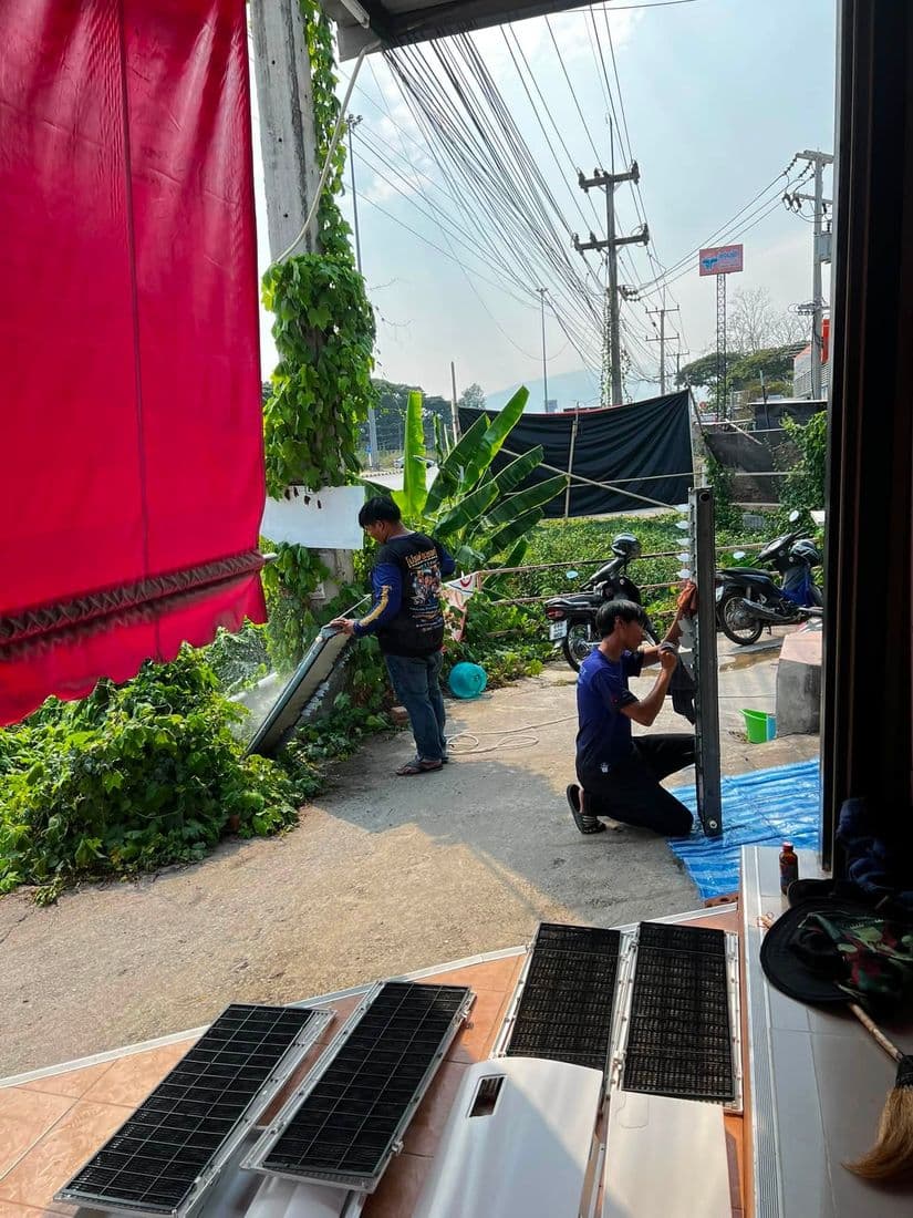 ช่างสองคนล้างชิ้นส่วนแอร์ในซอยหน้าร้าน โดยวางเรียงไว้บนพื้นกระเบื้อง