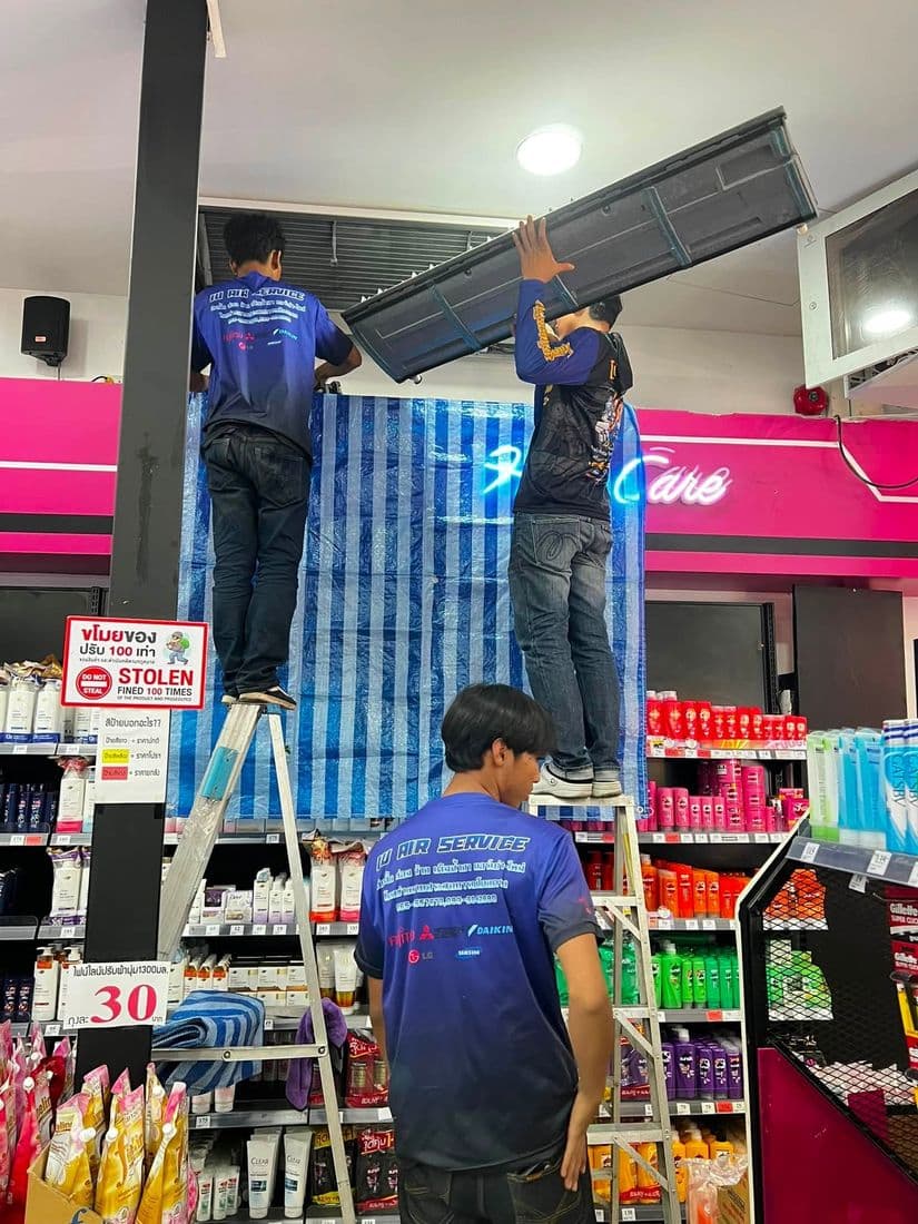 ช่างบนบันไดยกคอยล์เย็นลงจากผนังร้าน ขณะอีกคนคอยรับอยู่ด้านล่าง