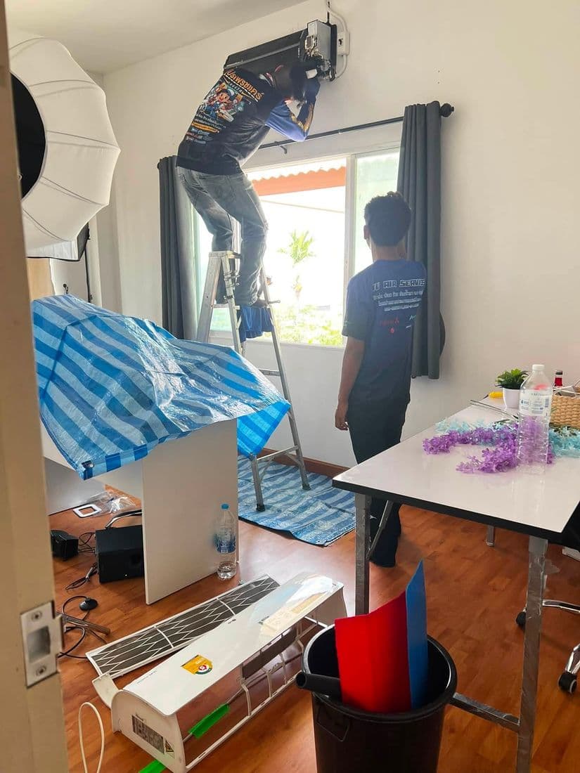 ช่างขึ้นบันไดถอดแอร์ในห้องที่ปูผ้าใบคลุมโต๊ะและข้าวของไว้ทั้งหมด