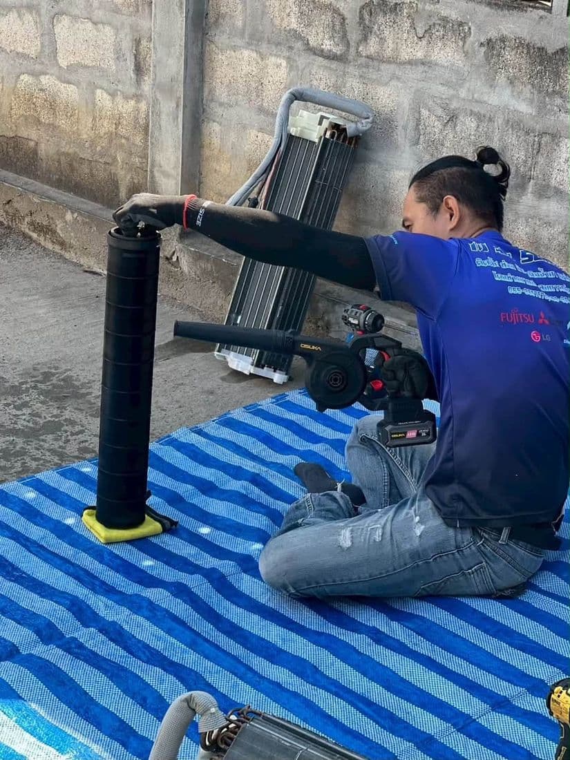 ช่างนั่งฉีดน้ำล้างชุดใบพัดโบลเวอร์ที่ตั้งอยู่บนผ้าใบ ข้างกำแพงหิน