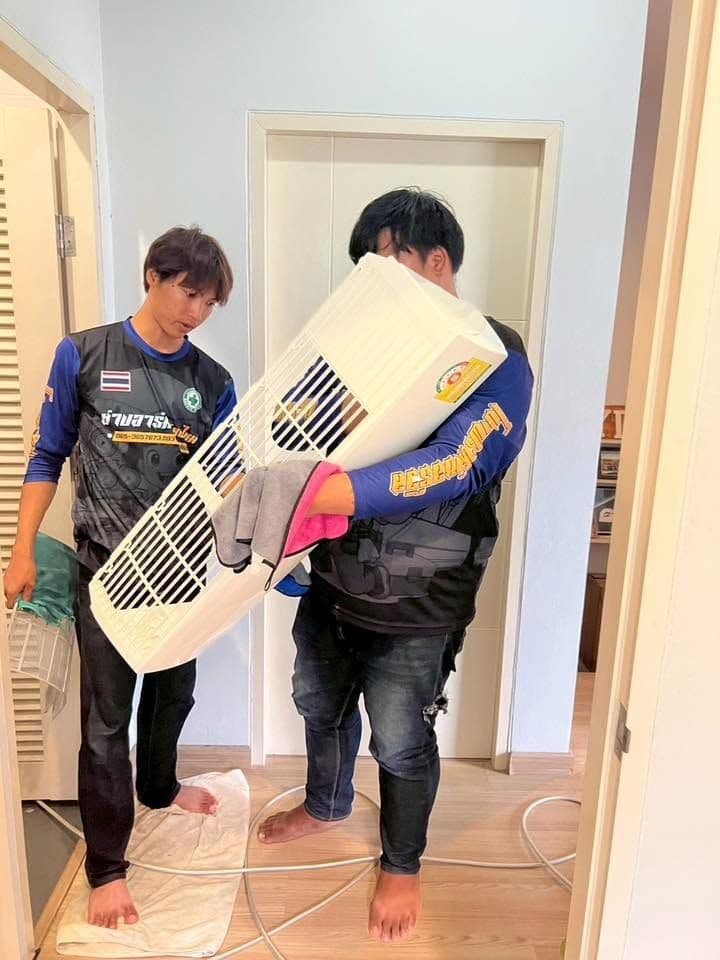 ช่างสองคนช่วยกันยกฝาครอบแอร์ในห้องพื้นกระเบื้อง ข้างประตูไม้