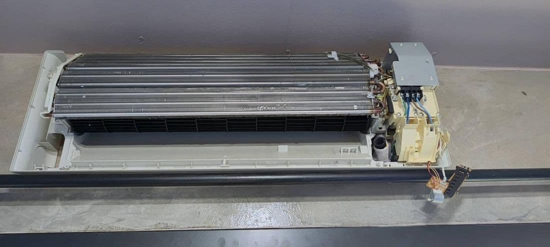 ตัวเครื่องแอร์ที่ถอดฝาออกวางบนพื้น เห็นแผงคอยล์และชุดสายไฟด้านใน