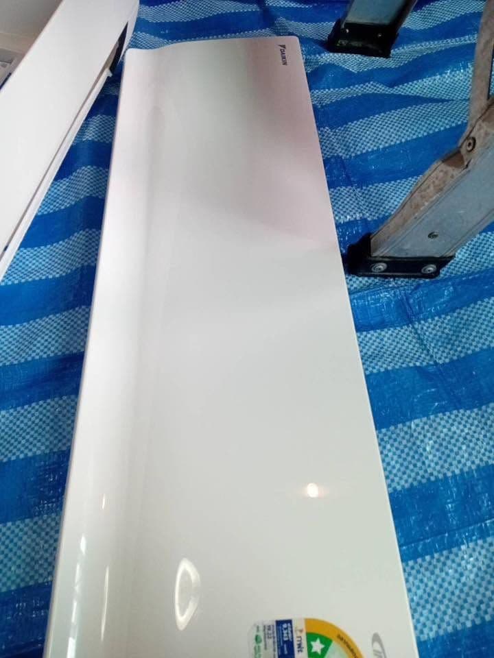 ฝาครอบแอร์ทรงยาวสีขาววางบนผ้าใบลายทางฟ้าขาวที่ปูรองพื้นห้อง