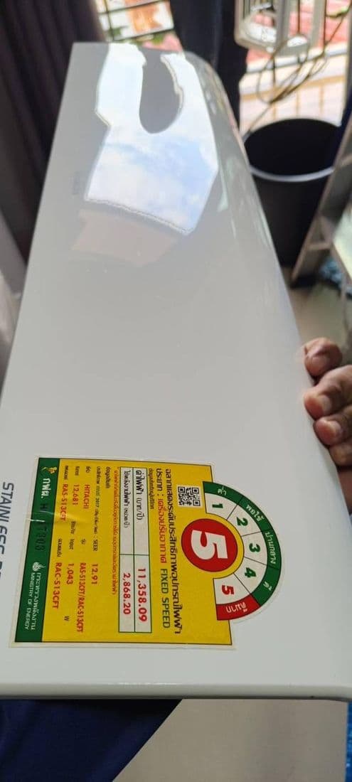 ฝาหน้าแอร์สีขาวติดสติกเกอร์ฉลากประหยัดไฟ ถือตั้งขึ้นก่อนนำไปล้าง