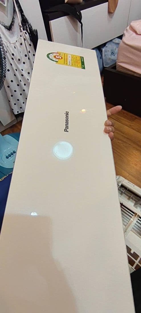 ฝาหน้าแอร์สีขาววางพิงข้างตัวเครื่องบนพื้นไม้ รอประกอบกลับหลังล้างเสร็จ