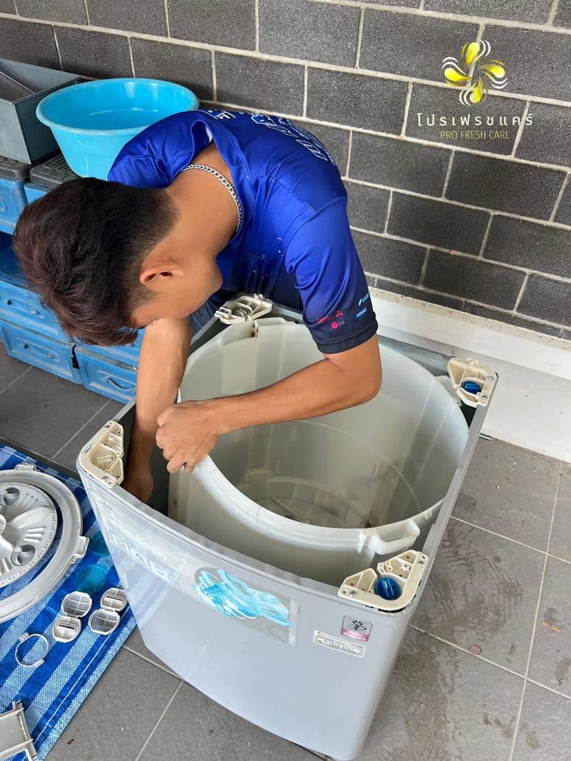 ช่างก้มล้วงล้างถังในเครื่องฝาบนที่ตั้งอยู่ในห้องน้ำผนังกระเบื้อง มีกะละมังฟ้าวางข้าง