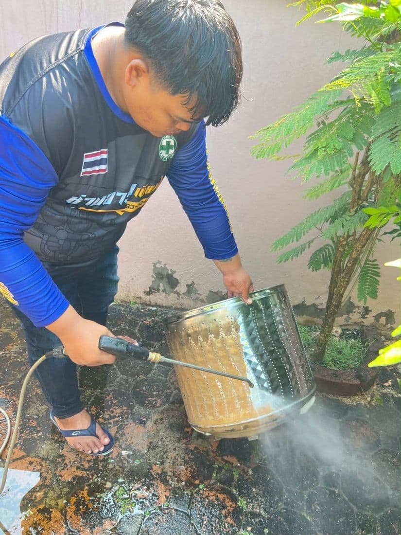 ช่างฉีดน้ำแรงดันล้างถังซักที่ยกเอียงกลางลานข้างกำแพงบ้าน