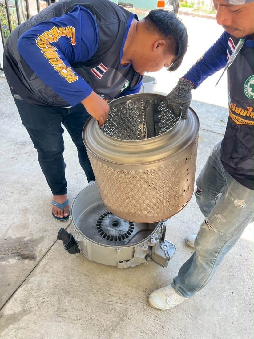 ช่างสองคนช่วยกันวางถังซักลงบนชุดมอเตอร์ ระหว่างประกอบกลับคืน