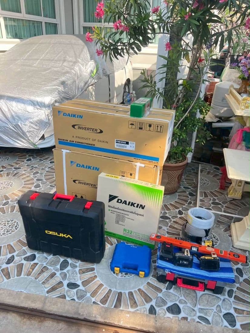 กล่องเครื่องใหม่ กล่องเครื่องมือ และอุปกรณ์เดินท่อ วางรวมกันในลานบ้านที่มีต้นไม้