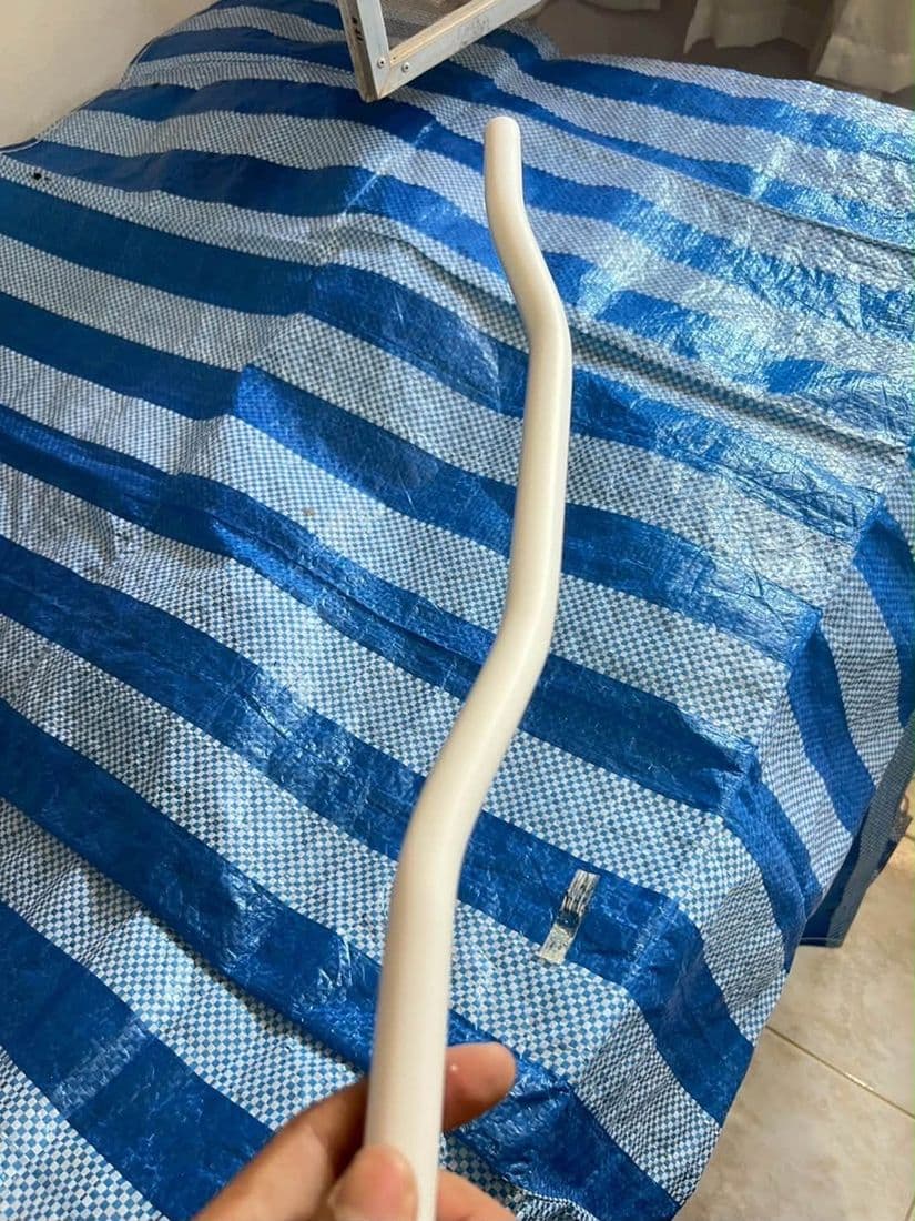 มือช่างดัดท่อน้ำทิ้งสีขาวให้ได้แนวโค้ง บนผ้าใบลายฟ้าขาวที่ปูรองไว้