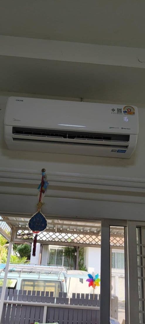 แอร์ติดผนังในห้องที่มองเห็นระเบียงและถนนหน้าบ้านผ่านหน้าต่างกระจก