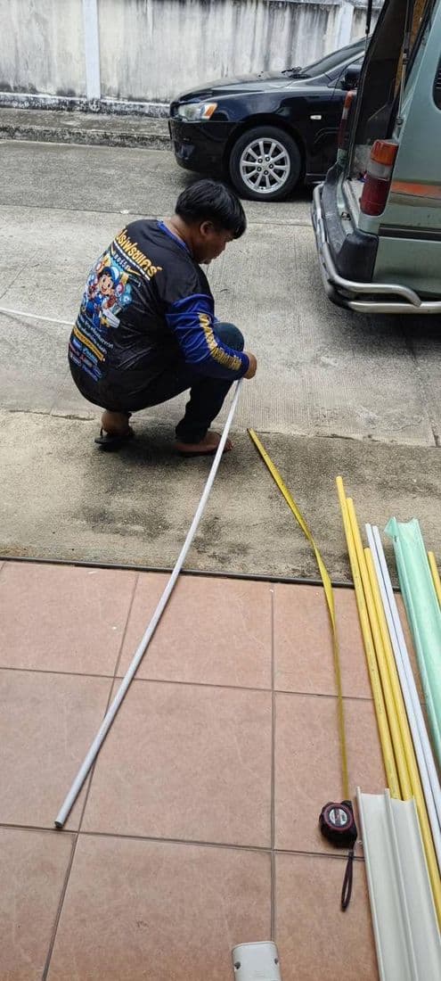 ช่างนั่งยองวัดความยาวรางครอบท่อบนพื้นลานจอดรถ ก่อนตัดเข้างาน