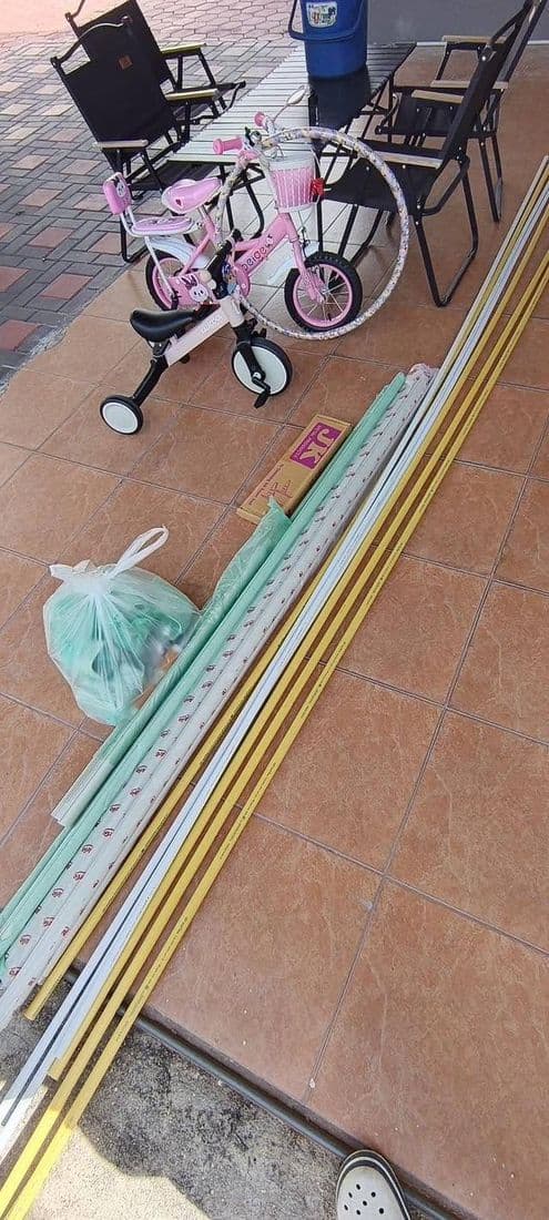 รางครอบท่อสีขาวเส้นยาววางเรียงบนพื้นกระเบื้อง ข้างจักรยานเด็กสีชมพู