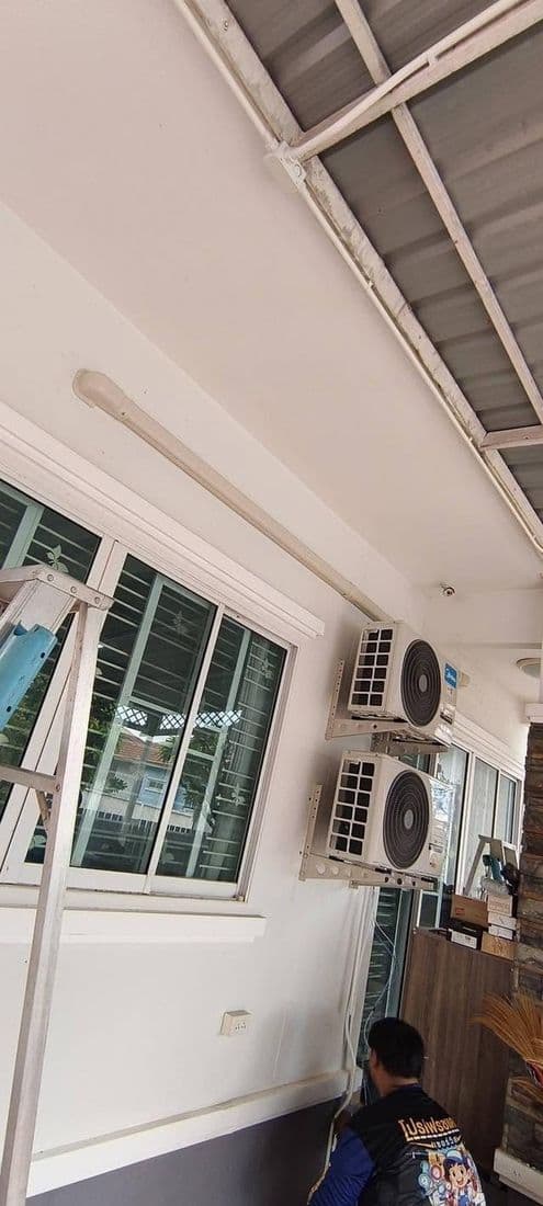 มุมห้องโล่งที่มีทั้งแอร์ติดผนังและคอยล์ร้อนติดตั้งใกล้กัน ใต้หลังคาโครงเหล็ก