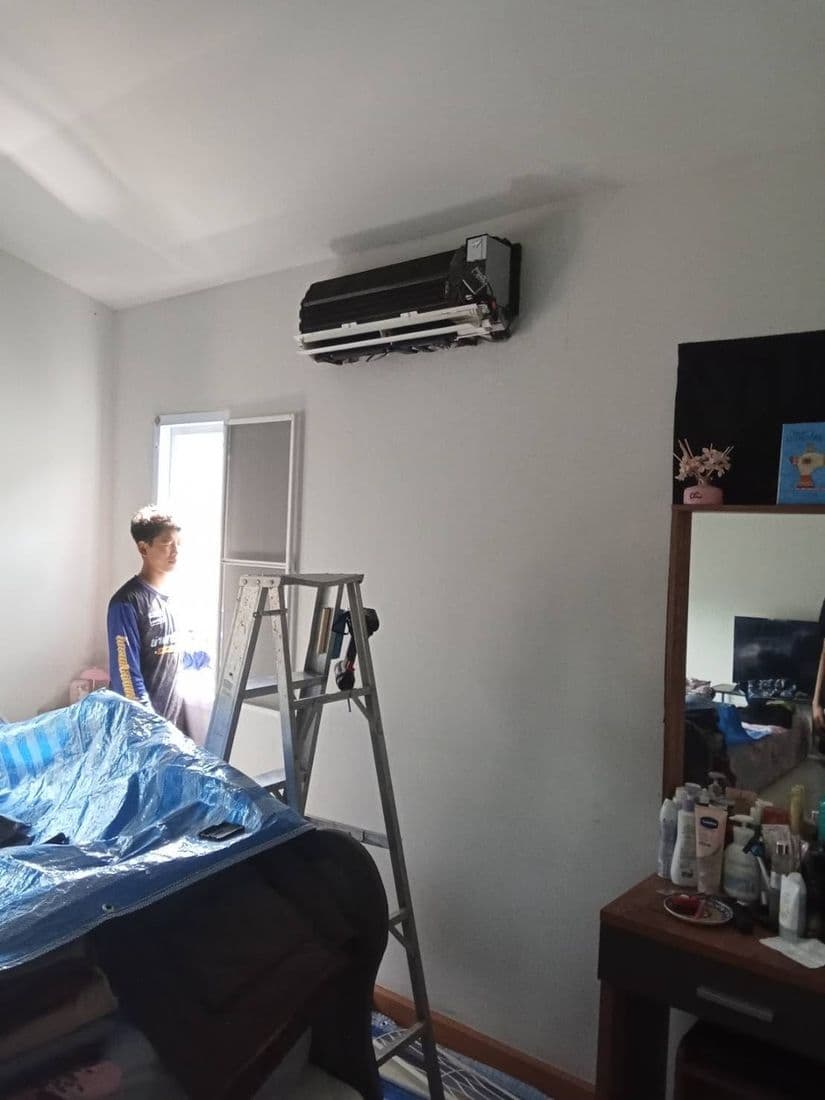 ห้องนอนที่มีเครื่องปรับอากาศติดผนัง และบันไดตั้งรอทำงานอยู่ข้างเตียง