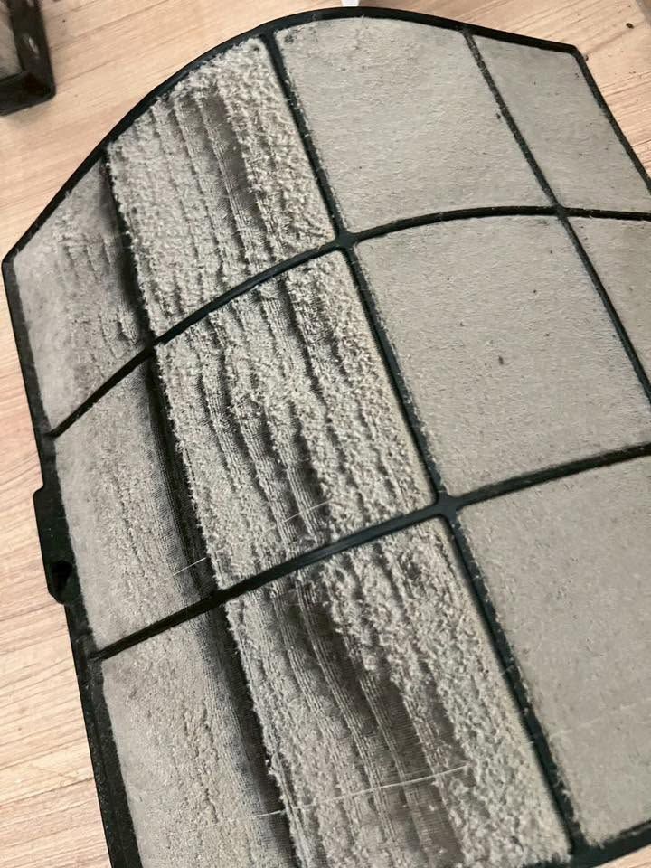 Close-up of an air filter caked with fluffy dust along the mesh, photographed before cleaning