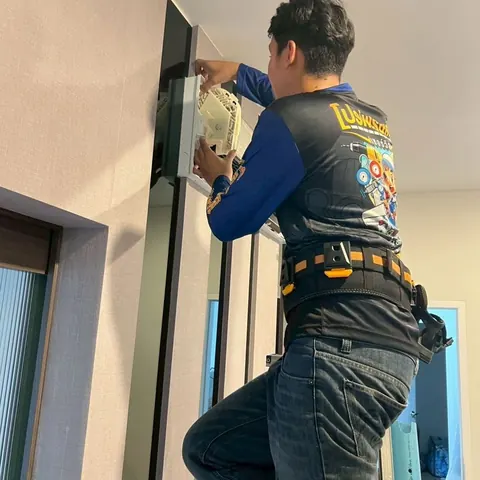 ช่างกำลังถอดหน้ากากแอร์ติดผนังลงจากเครื่องในห้องนอน