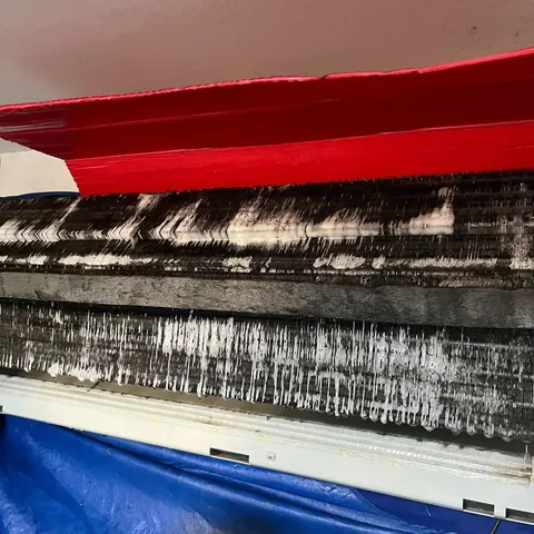 Close-up inside an indoor unit before cleaning, showing black grime built up in long streaks across the surface