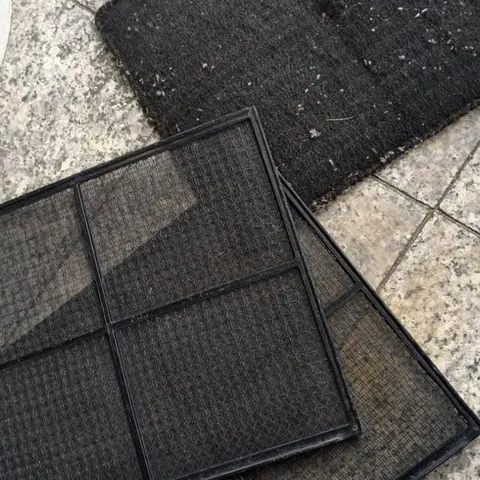 Two aircon filter screens lifted out and set down on a tiled floor, with grey dust visible across the mesh