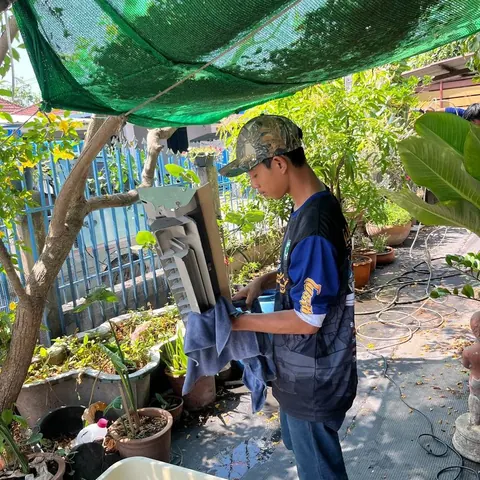 ช่างล้างชิ้นส่วนกลางสวนใต้ตาข่ายพรางแสงสีเขียว มีกะละมังรองน้ำอยู่ข้างตัว