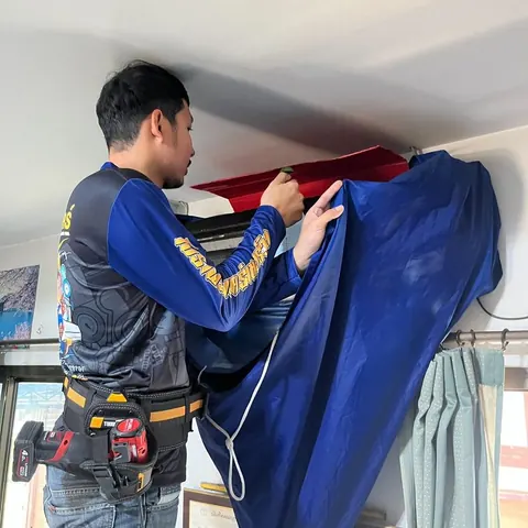 ช่างขึงผ้ากันน้ำสีน้ำเงินใต้ตัวเครื่องบนผนัง ก่อนเริ่มฉีดล้างในห้อง
