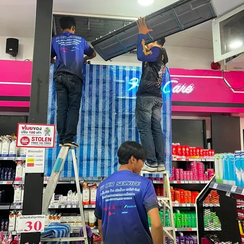 ช่างบนบันไดยกคอยล์เย็นลงมา ขณะอีกคนคอยรับอยู่ด้านล่าง