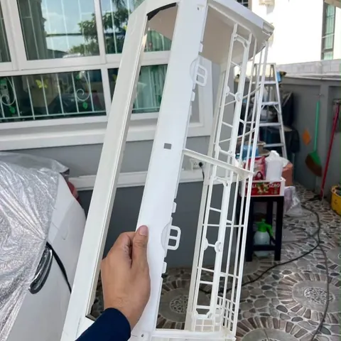 ช่างประคองฝาครอบแอร์สีขาวที่ล้างเสร็จแล้วเอาไว้ในมือ
