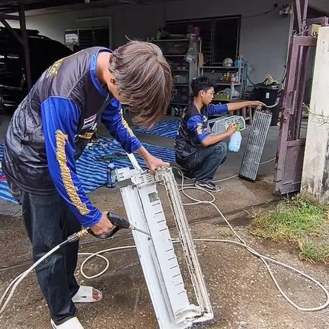 ช่างก้มลงฉีดน้ำล้างชิ้นส่วนแอร์ที่ถอดมาวางเตรียมไว้