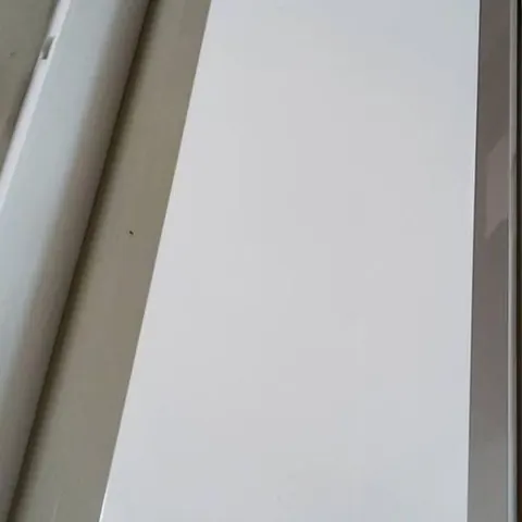 ฝาครอบแอร์ทรงยาวพิงผนังอยู่ในห้อง มีสติกเกอร์ฉลากติดที่มุมด้านล่าง