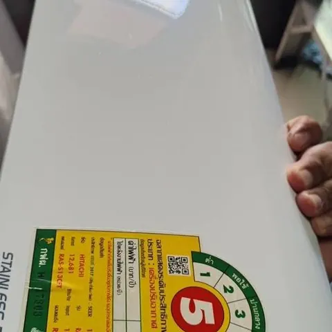 ฝาหน้าแอร์สีขาวติดสติกเกอร์ฉลากประหยัดไฟ ถือตั้งขึ้นก่อนนำไปล้าง