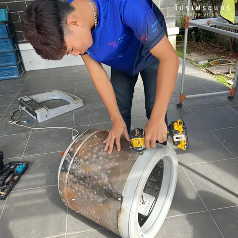 ช่างก้มขัดถังซักที่วางนอนอยู่ มีคราบน้ำตาลติดรอบตัวถังทั้งใบ