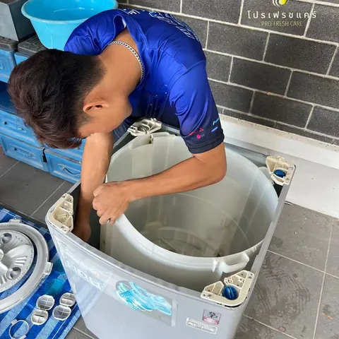 ช่างก้มล้วงเข้าไปล้างถังในเครื่องฝาบน มีกะละมังรองน้ำวางอยู่ข้าง
