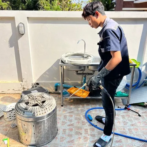 ช่างฉีดน้ำล้างชิ้นส่วน มีถังซักอีกสองใบตั้งรอคิวล้างอยู่