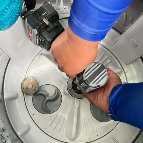 มือช่างใช้สว่านไฟฟ้าขันน็อตกลางถังเพื่อถอดจานซักออกจากแกน