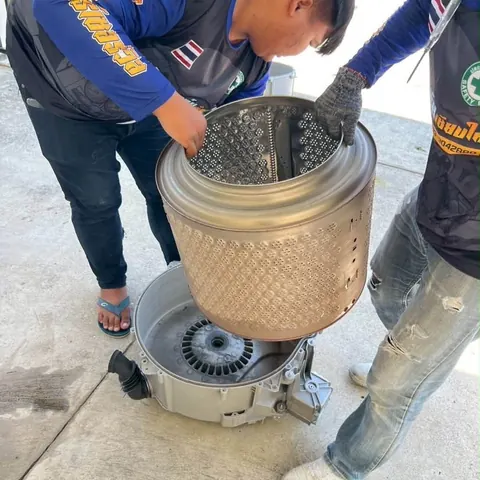 ช่างสองคนช่วยกันวางถังซักลงบนชุดมอเตอร์ ระหว่างประกอบกลับคืน