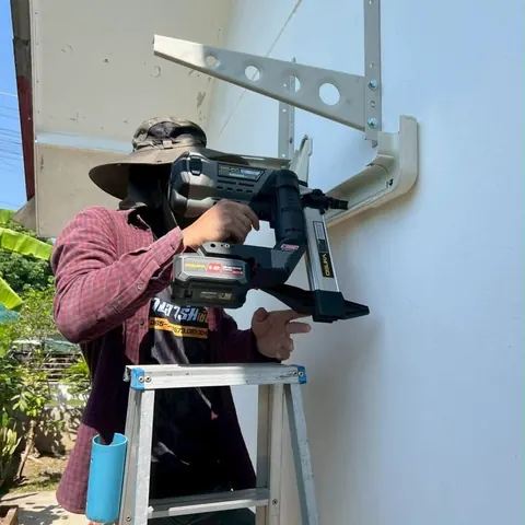 ช่างบนบันไดเจาะยึดขาเหล็กสำหรับแขวนคอยล์ร้อนเข้ากับจุดติดตั้ง
