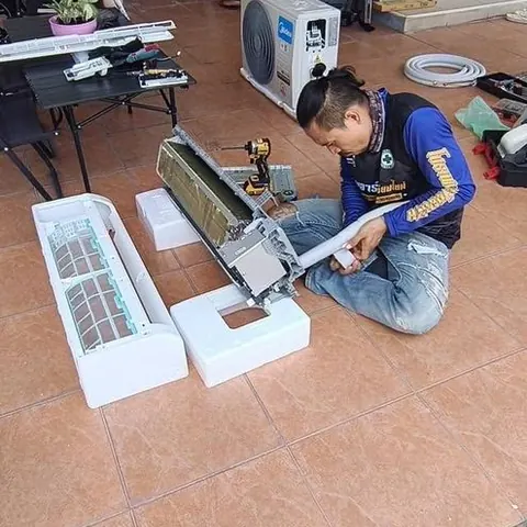 ช่างนั่งประกอบเครื่องบนพื้นลานหน้าบ้าน โดยมีอีกคนยืนดูอยู่ด้านหลัง